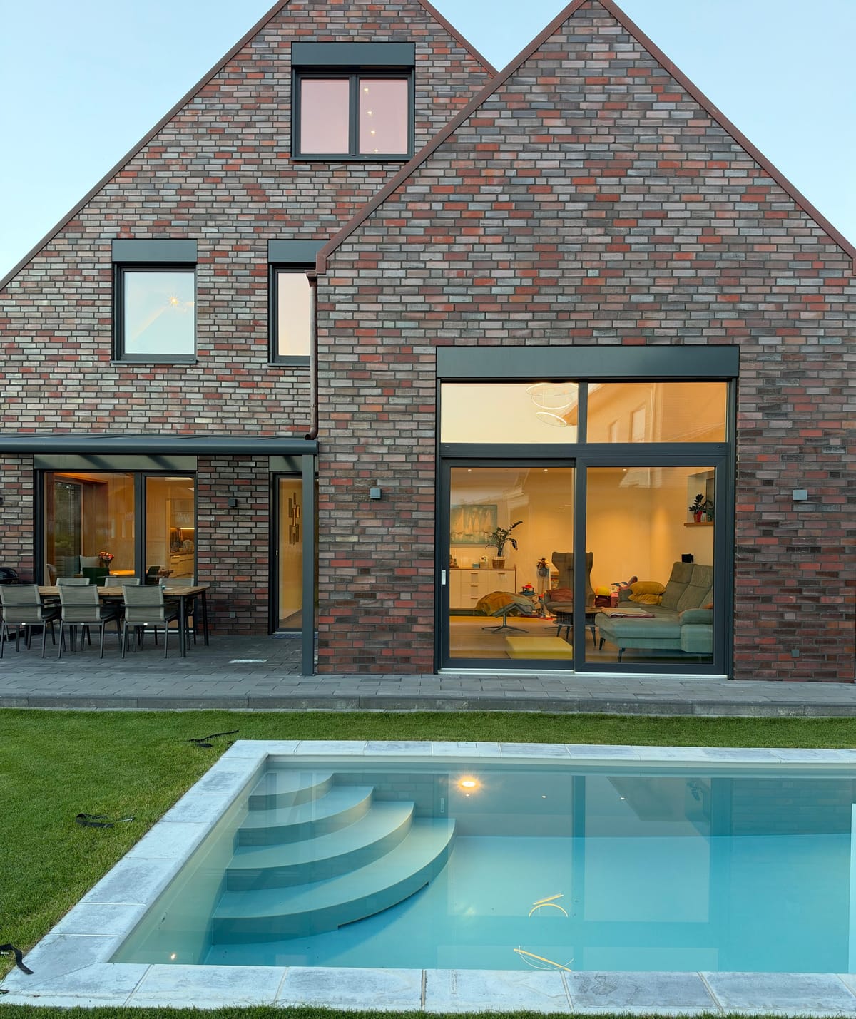 Unser Wohnhaus in Hörstel am Abend von der Gartenseite: Licht im Wohnzimmer, beleuchteter Pool im Vordergrund