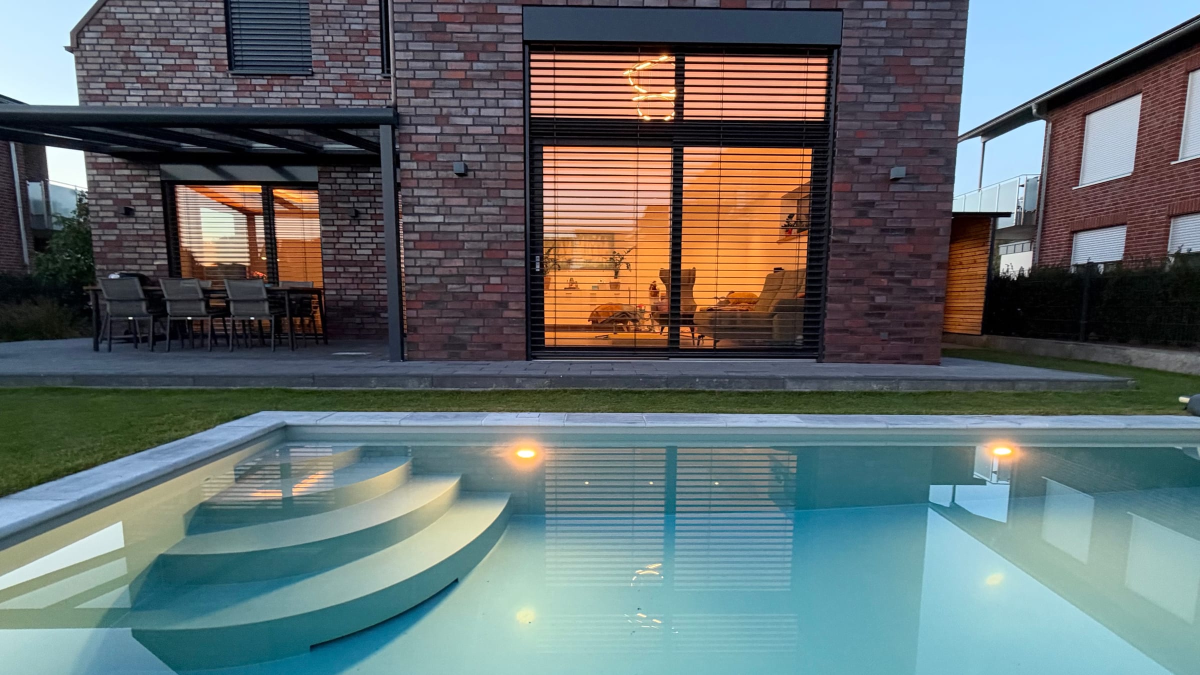 Unser Wohnhaus in Hörstel am Abend von der Gartenseite: Licht im Wohnzimmer, beleuchteter Pool im Vordergrund