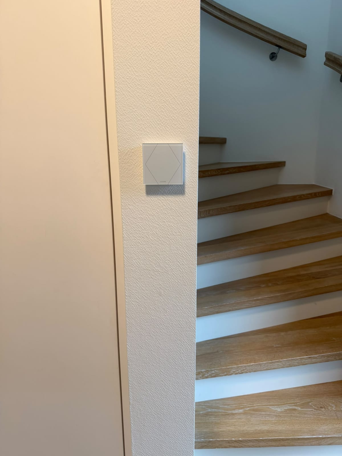 Weißer Loxone Touch Pure an der Wand neben einer Holztreppe in Laer